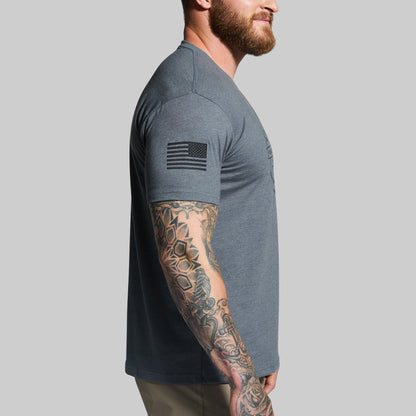 Man wearing a gray t-shirt with a tattooed arm on a plain background