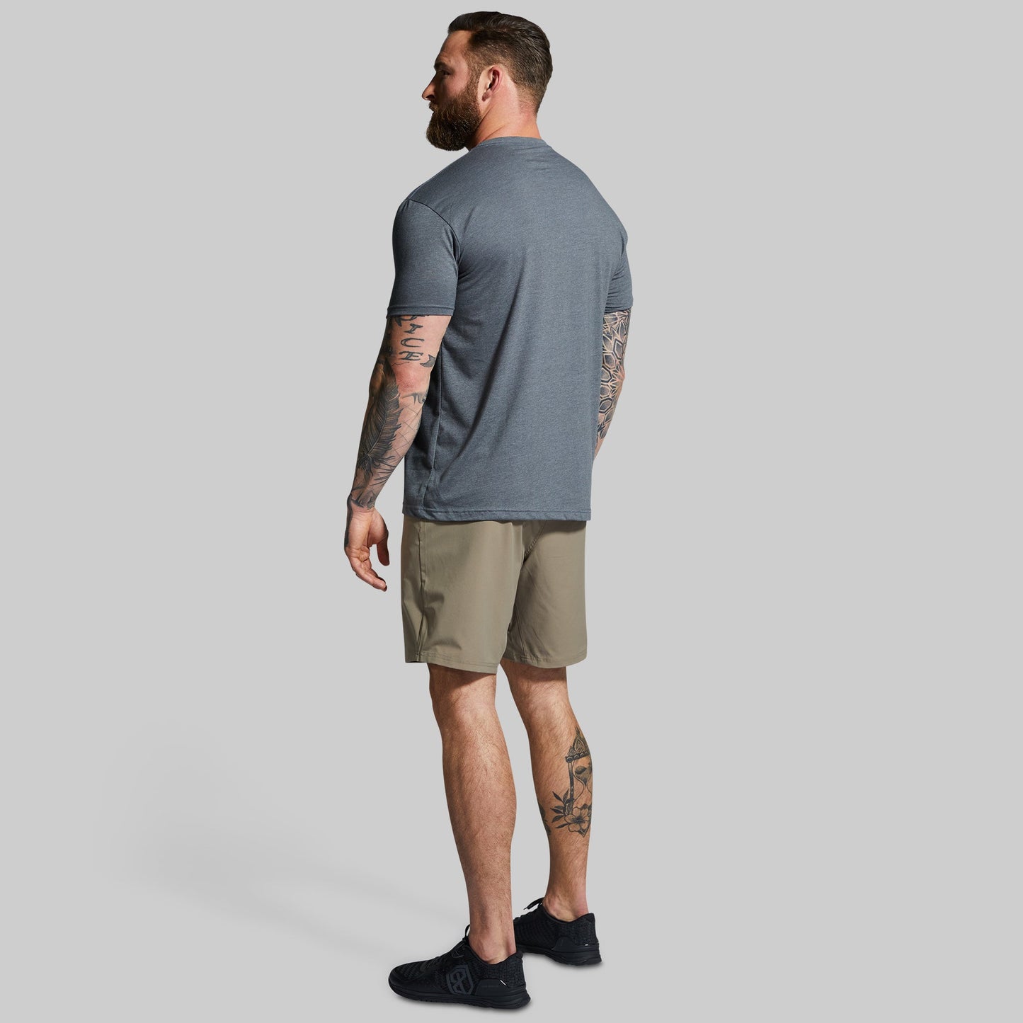 Man wearing a gray t-shirt and beige shorts on a plain background