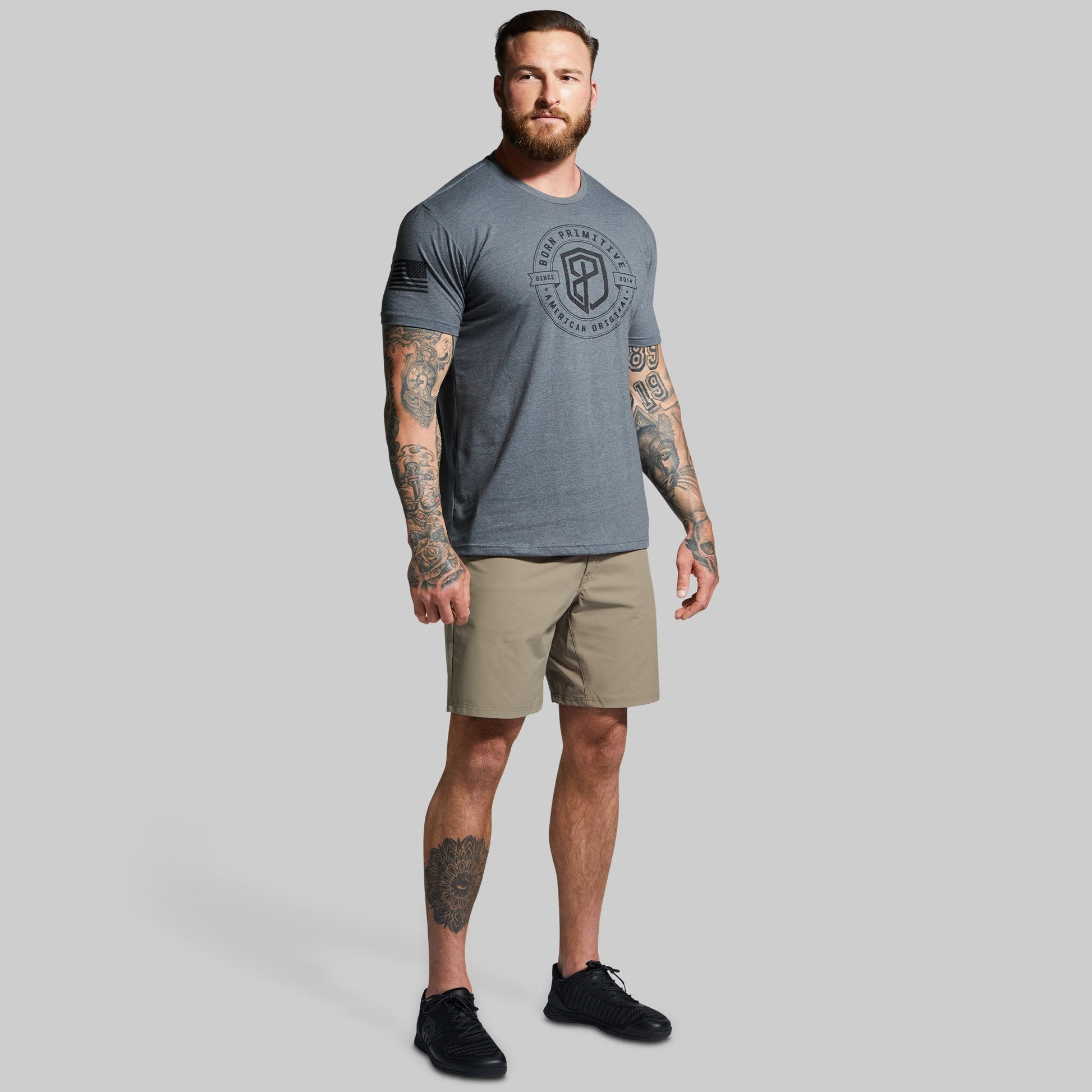 Man wearing a gray t-shirt with a logo and beige shorts on a gray background