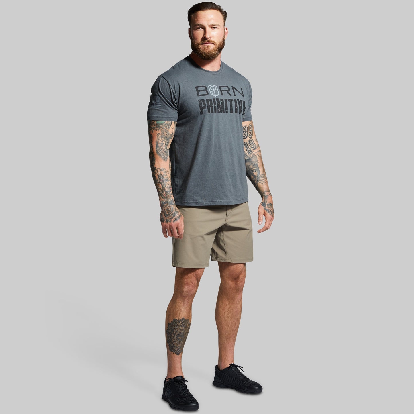 Man wearing a gray 'Born Primitive' t-shirt and beige shorts on a gray background