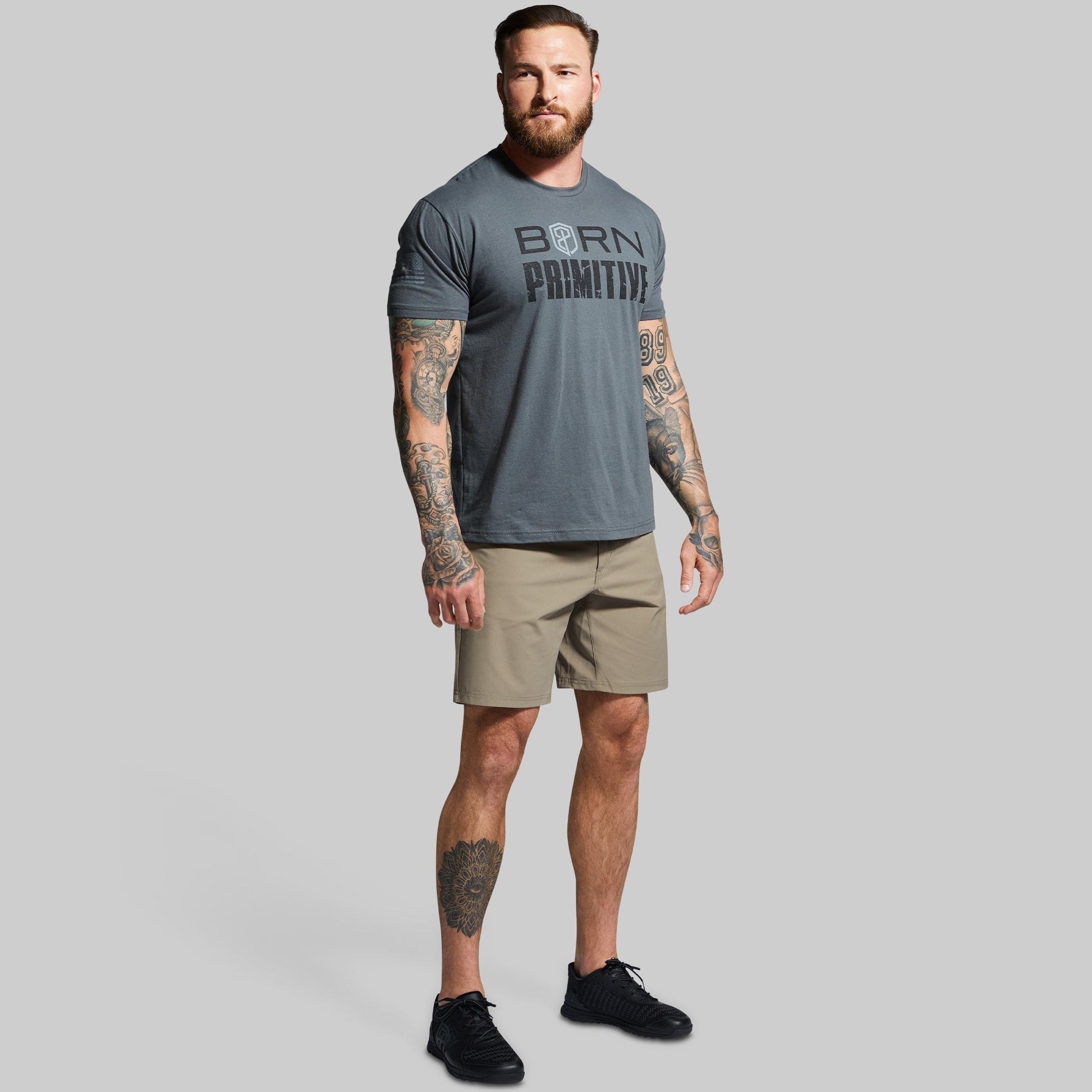 Man wearing a gray 'Born Primitive' t-shirt and beige shorts on a gray background