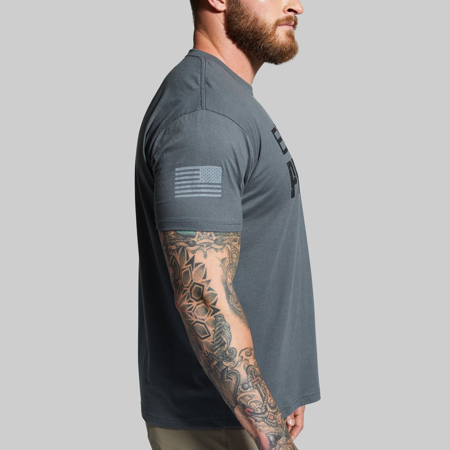 Man wearing a gray t-shirt with a tattooed arm on a gray background