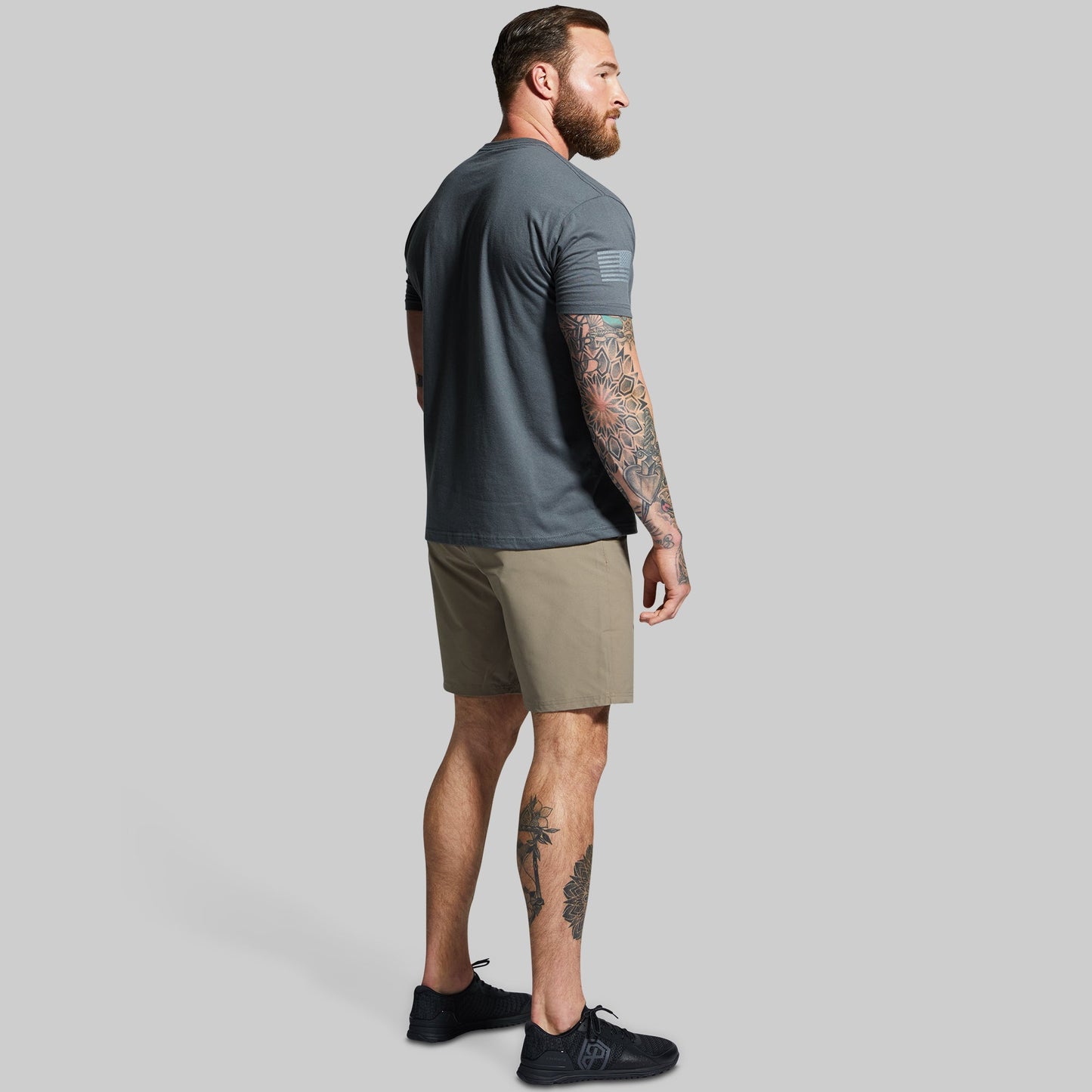 Man wearing a dark gray t-shirt and beige shorts on a gray background