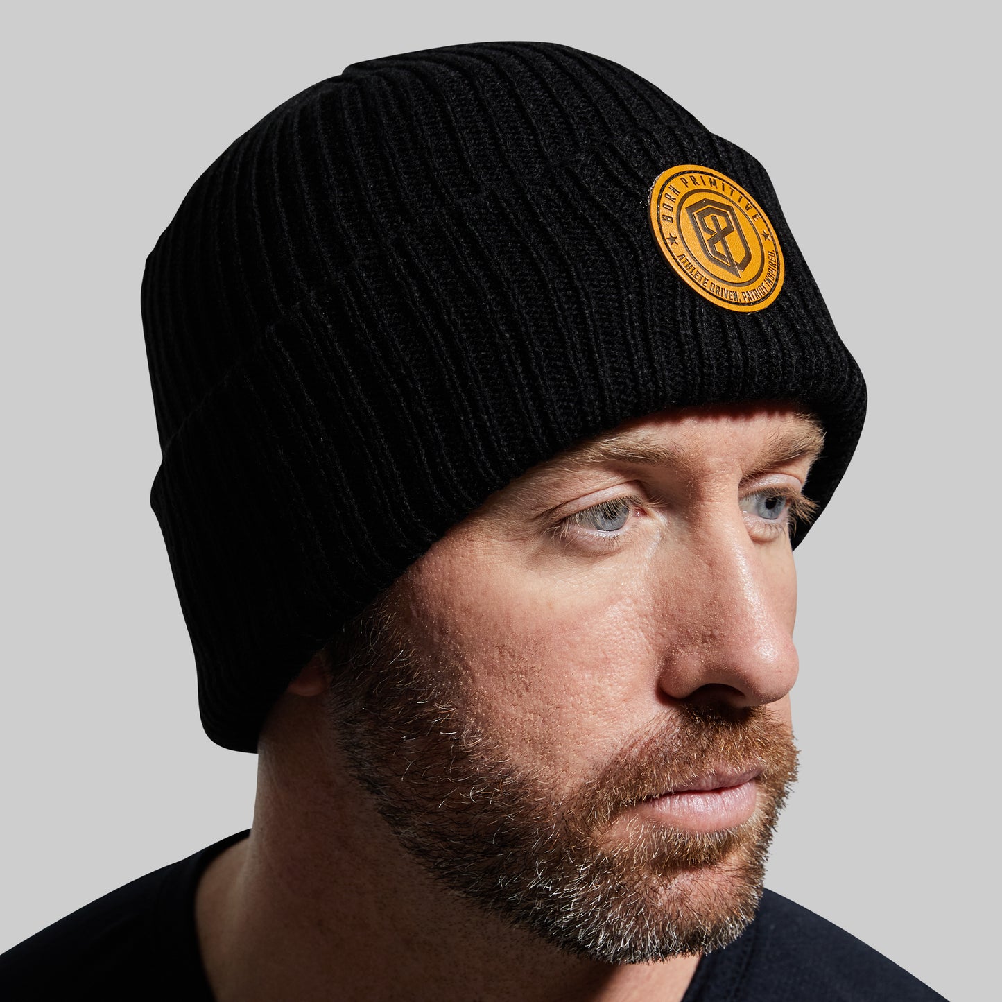 Man wearing a black beanie with a yellow logo against a gray background