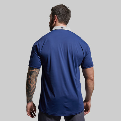 Man wearing a blue athletic polo on a gray background
