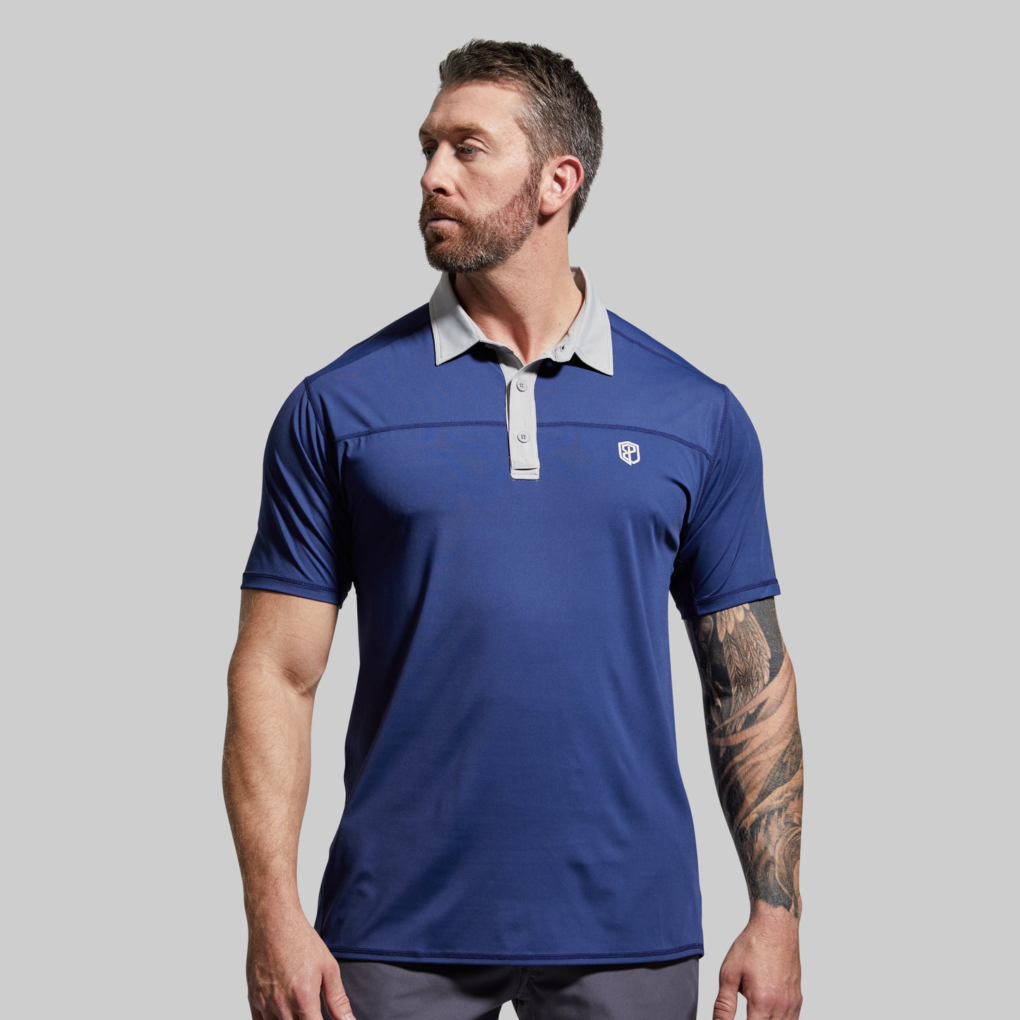 Man wearing a blue polo shirt with a white collar against a gray background