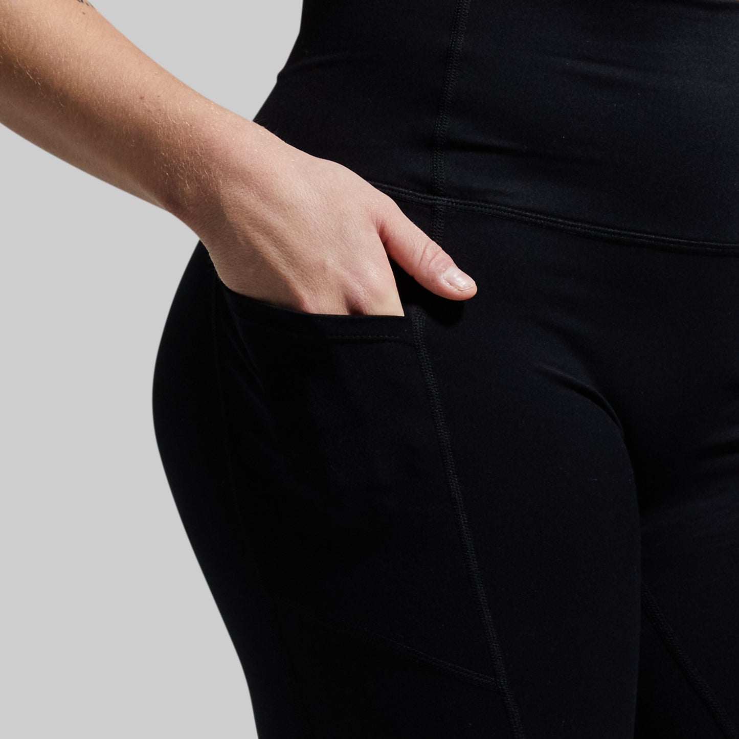 Person wearing black shorts with hand in pocket on a neutral background