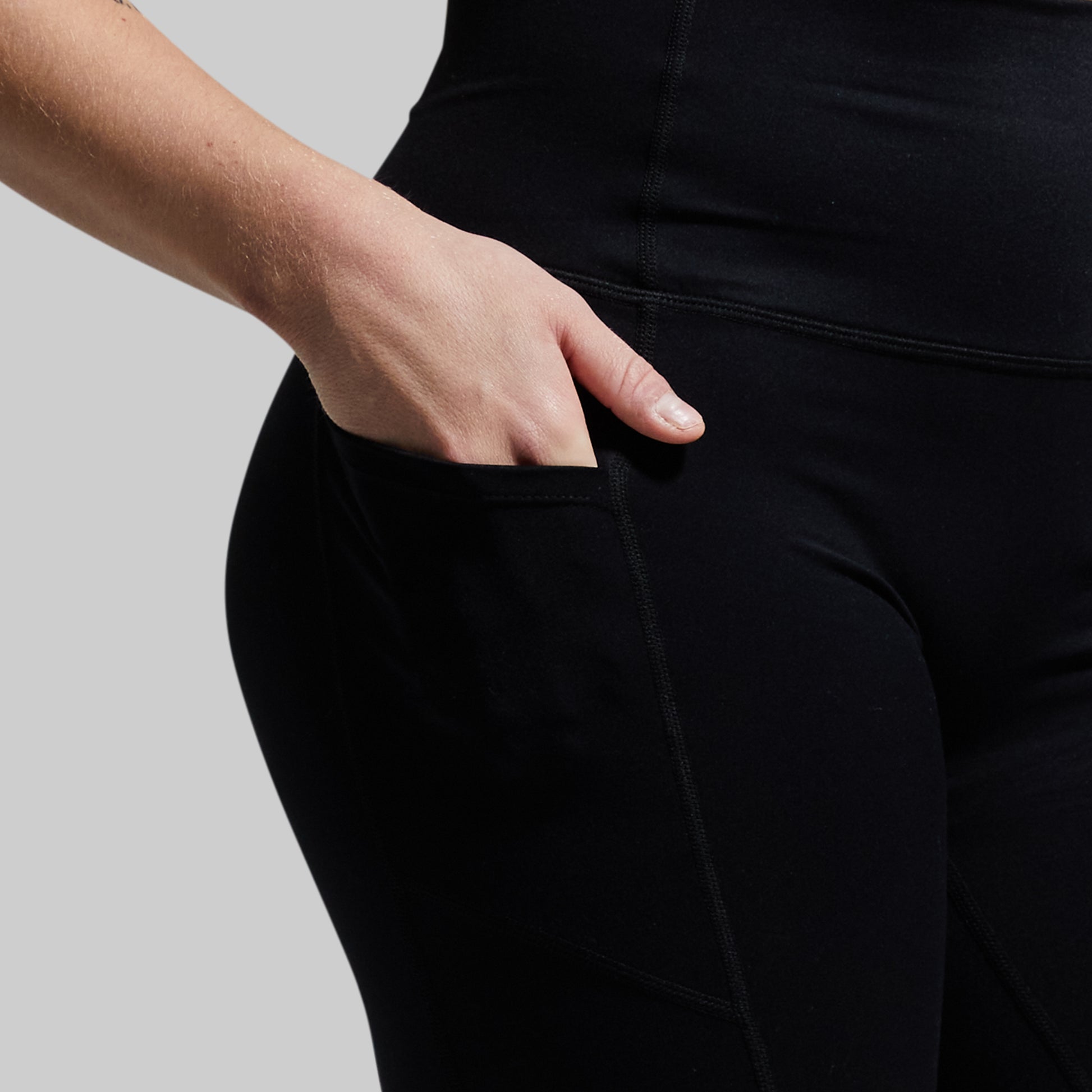Person wearing black shorts with hand in pocket on a neutral background