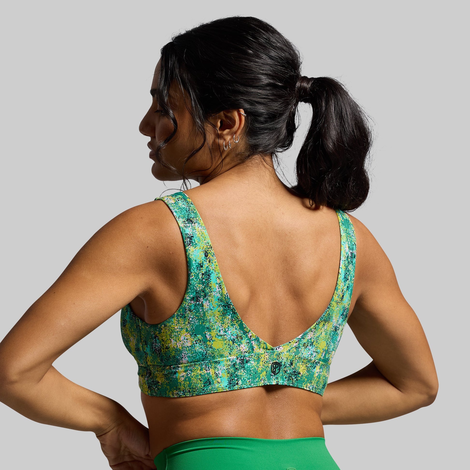 A woman wearing a green and multicolor floral sports bra with over-the-shoulder back straps, facing away from the camera.