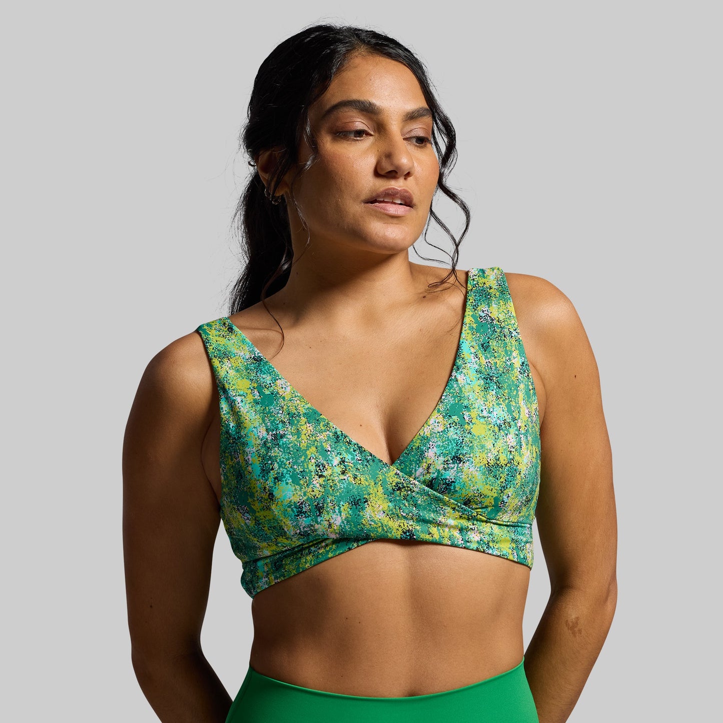 Woman wearing a green and yellow patterned sports bra against a gray background