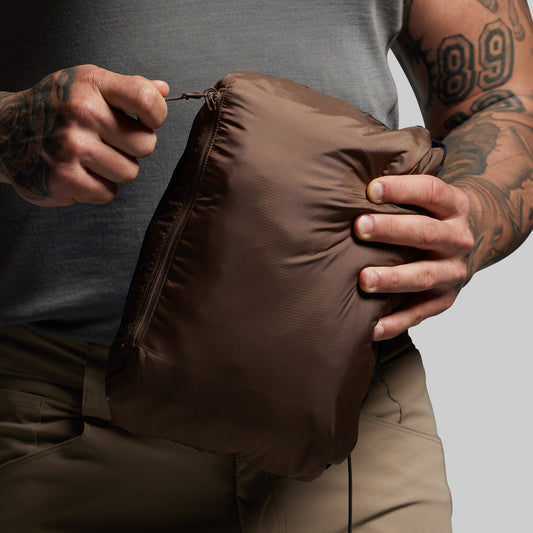 Person zipping up a brown jacket in travel pouch against a neutral background
