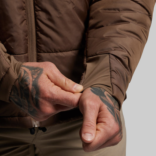 Close-up of a person wearing a brown jacket with tattooed hands.