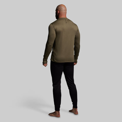 Man wearing a green long-sleeve shirt and black pants on a gray background