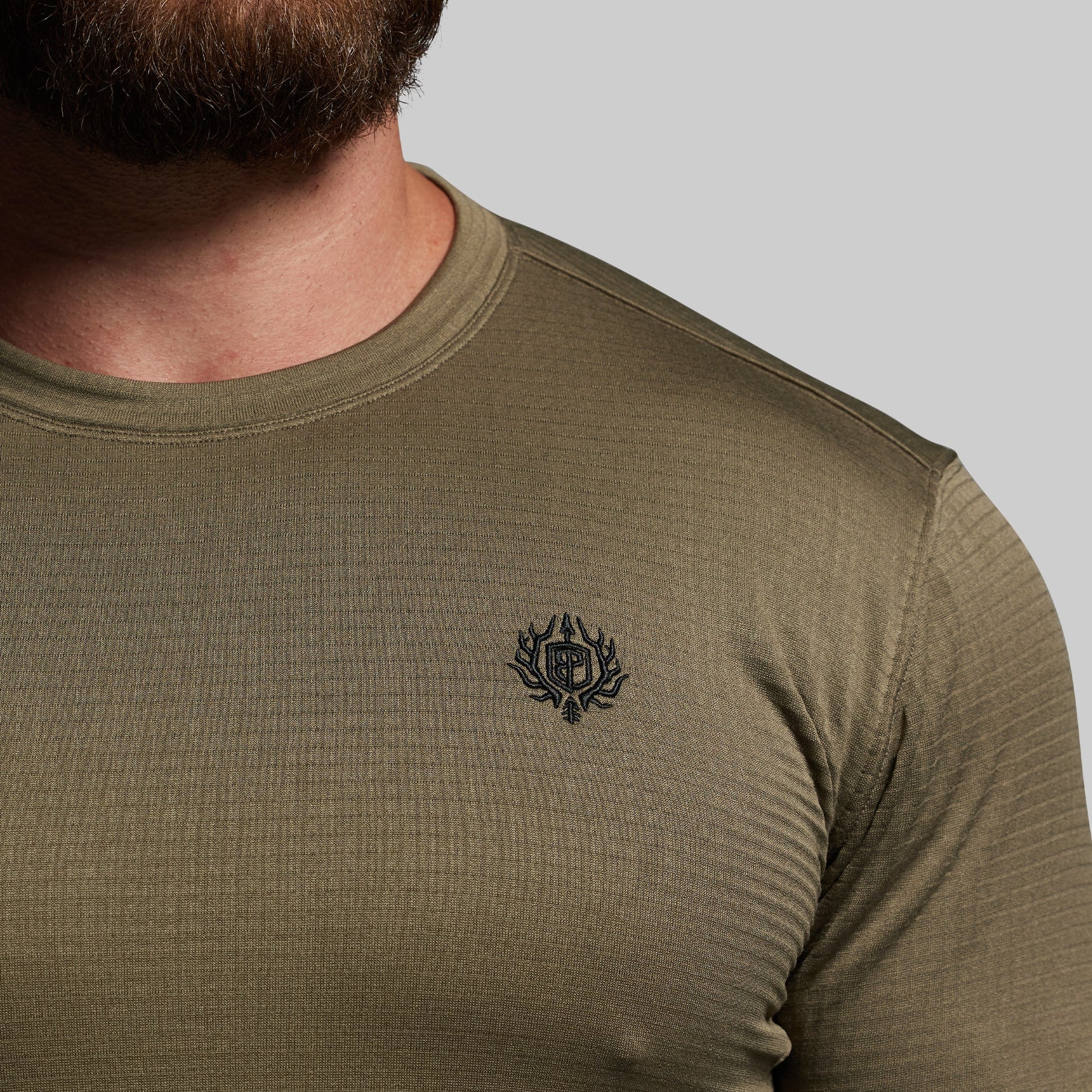 Olive green long-sleeve shirt with a logo on the chest against a neutral background