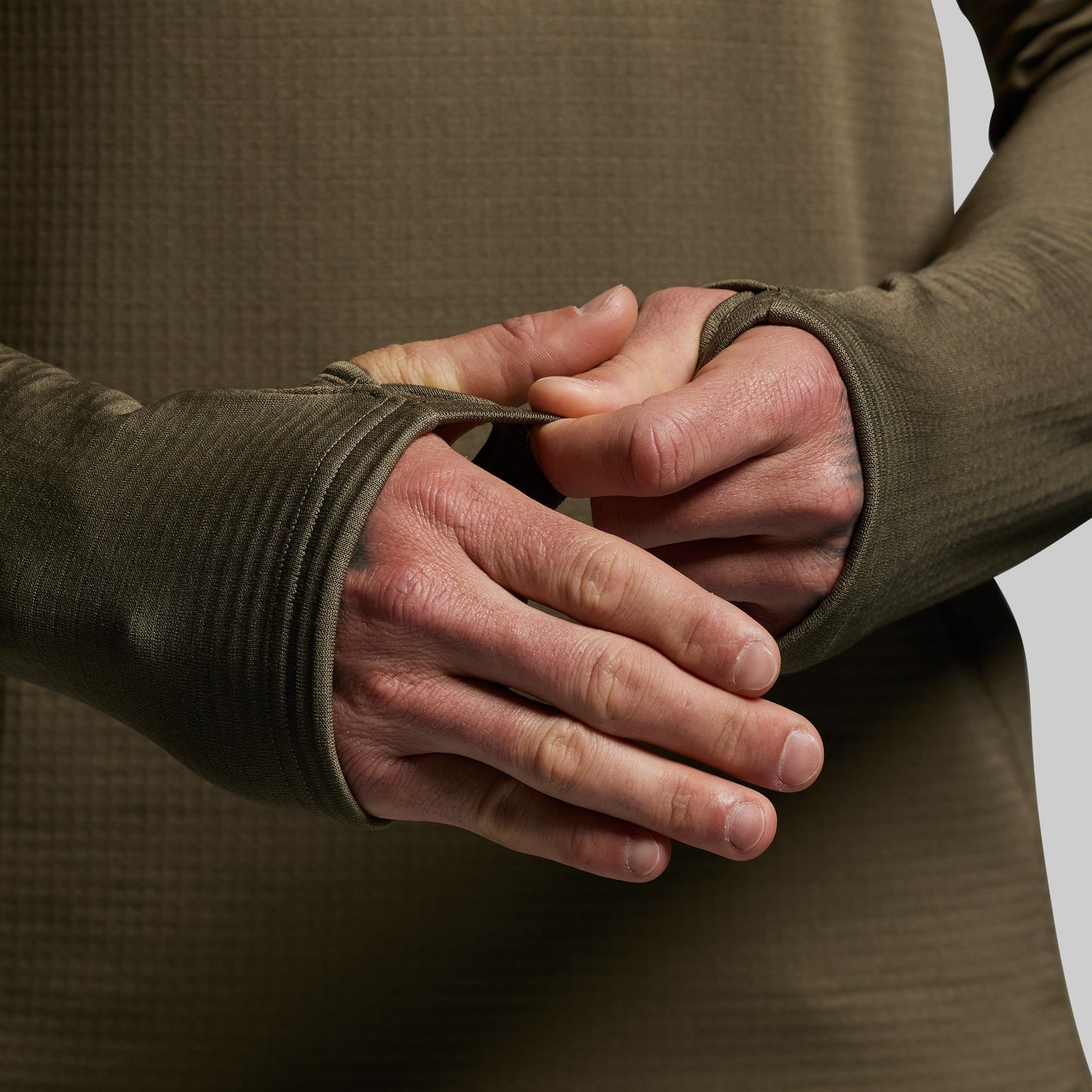 Close-up of a person wearing a green long-sleeve shirt with thumbholes over their hands.