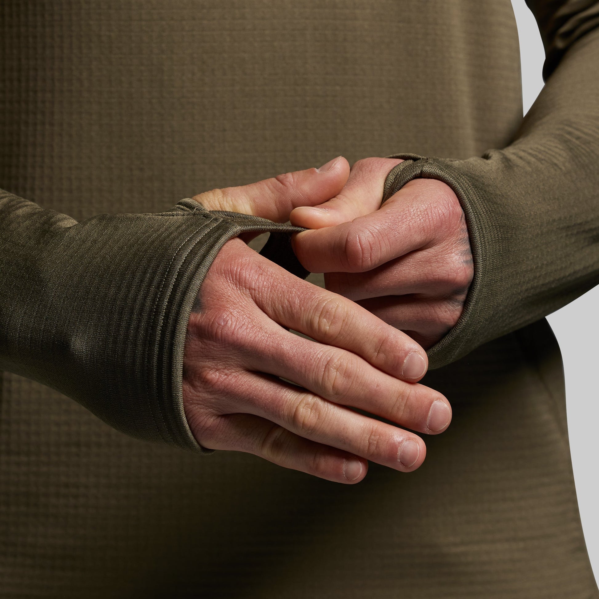 Close-up of a person wearing a green long-sleeve shirt with thumbholes over their hands.