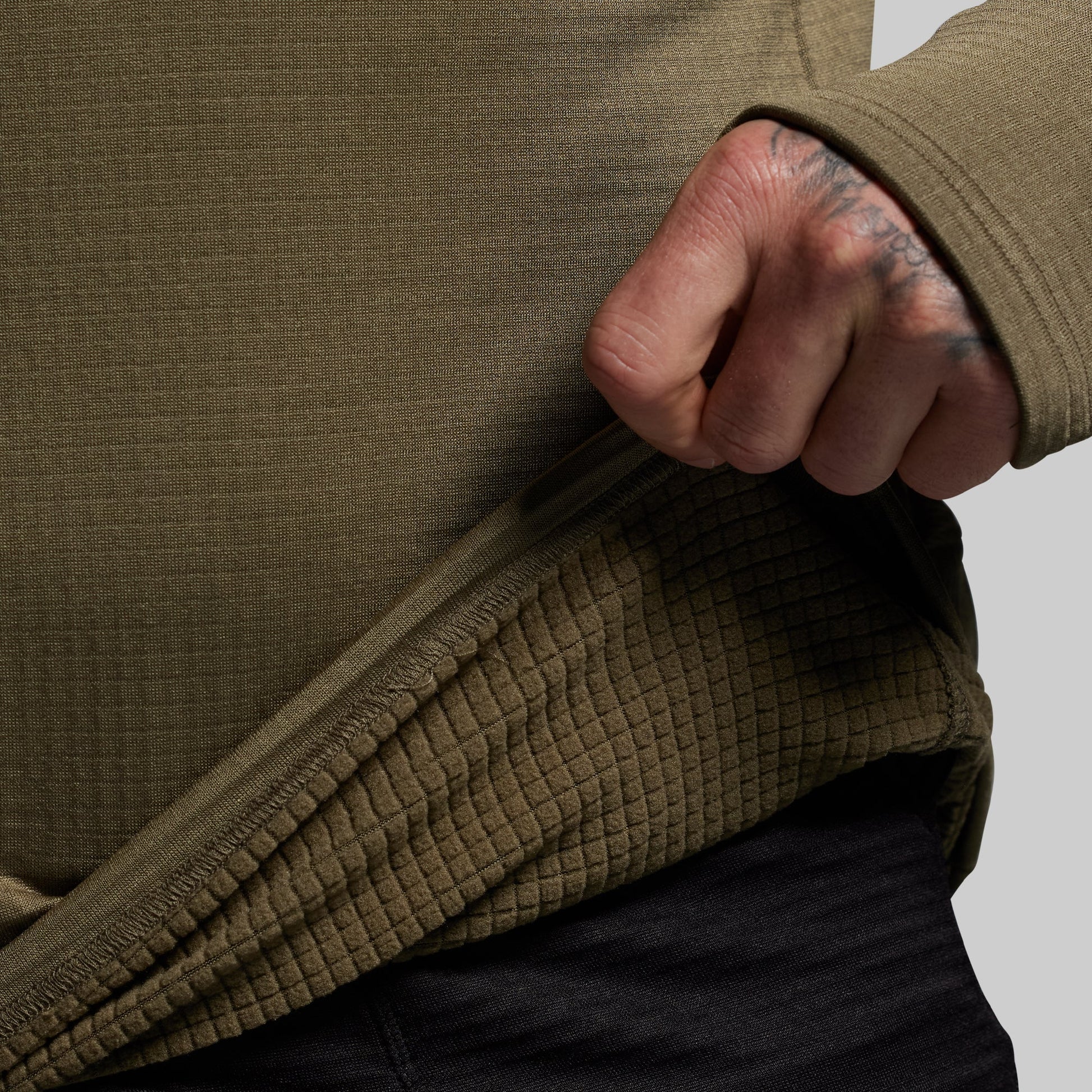 Person wearing a green base layer with a close-up of the inner lining on a gray background