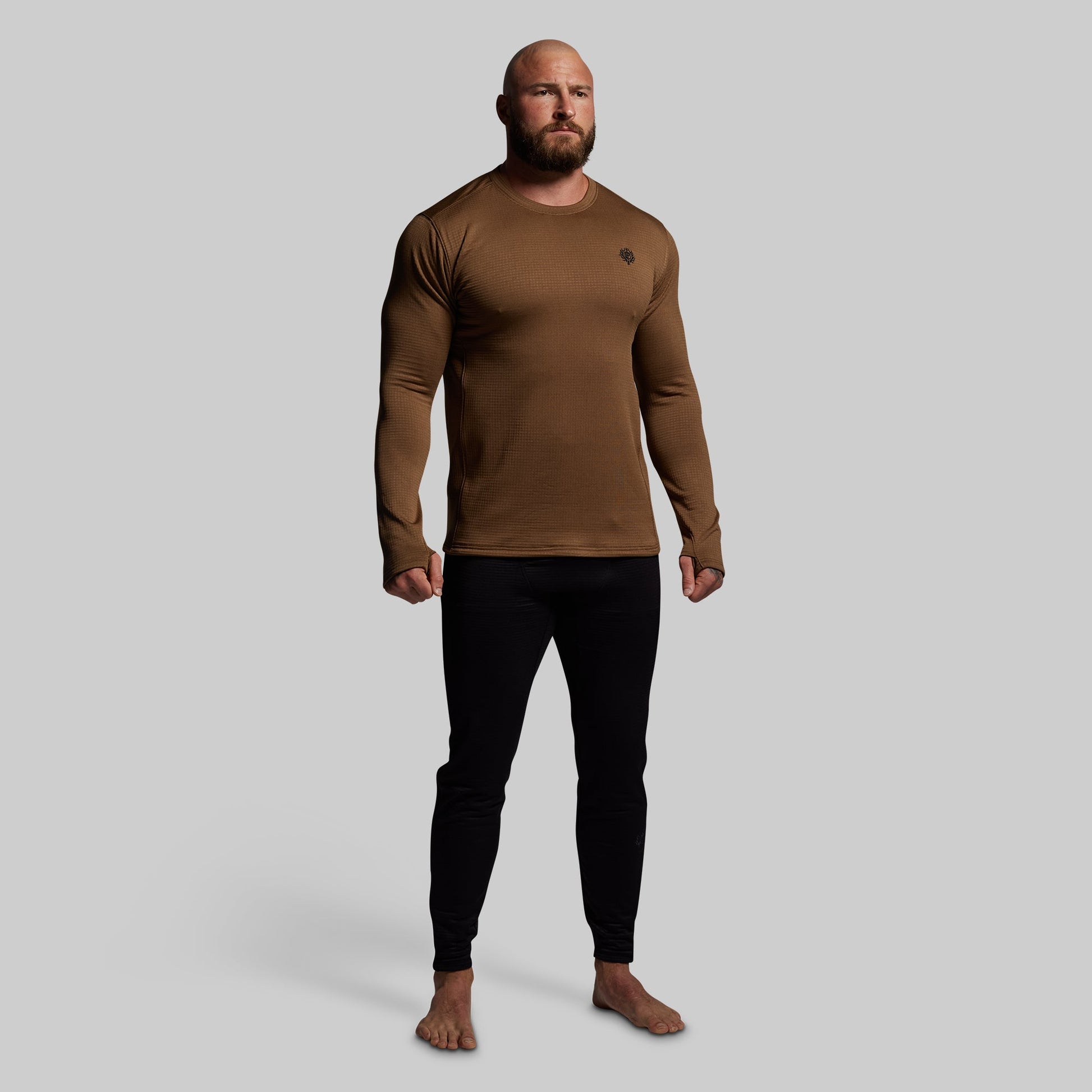 Man wearing a brown long-sleeve shirt and black pants on a gray background