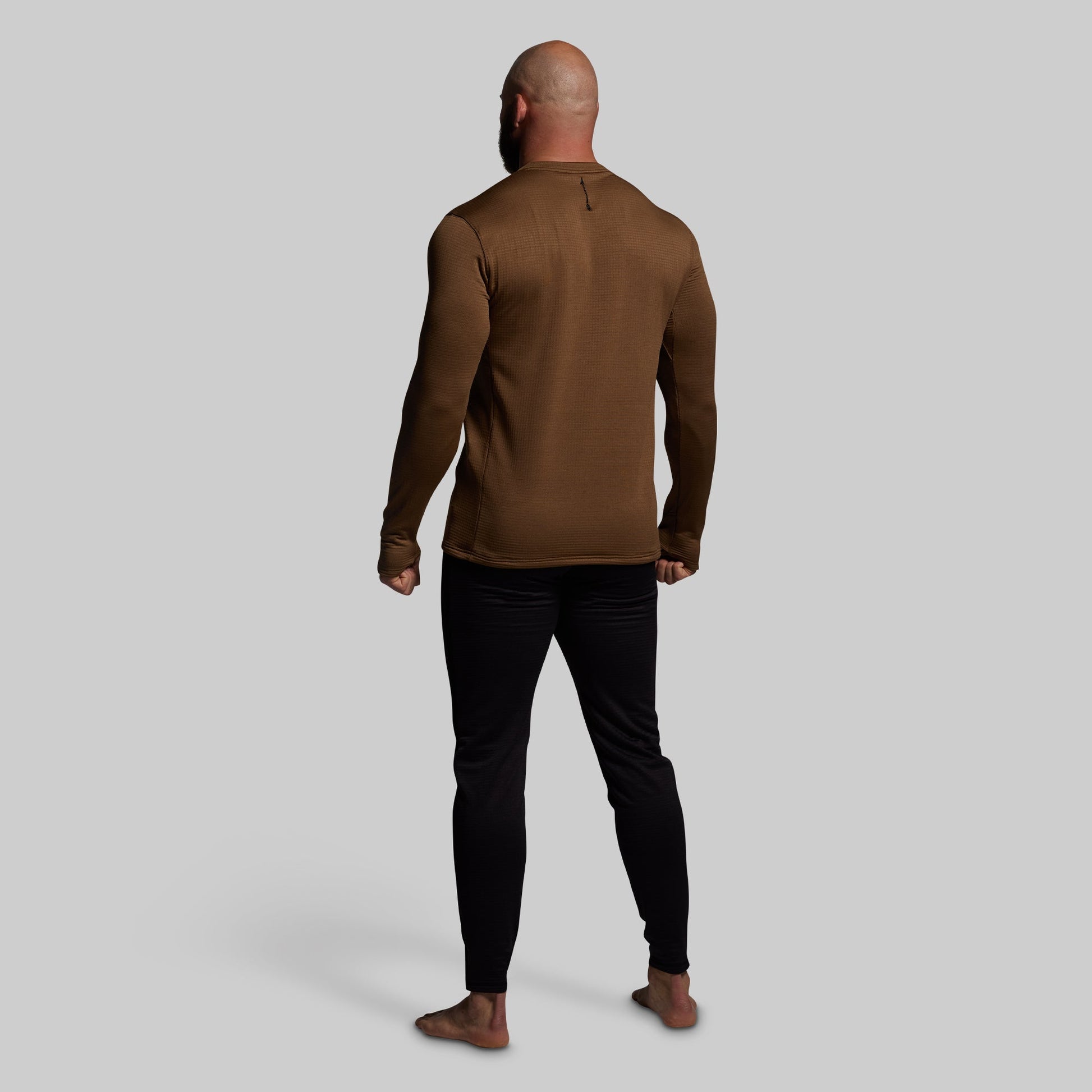 Man wearing a brown long-sleeve shirt and black pants on a gray background
