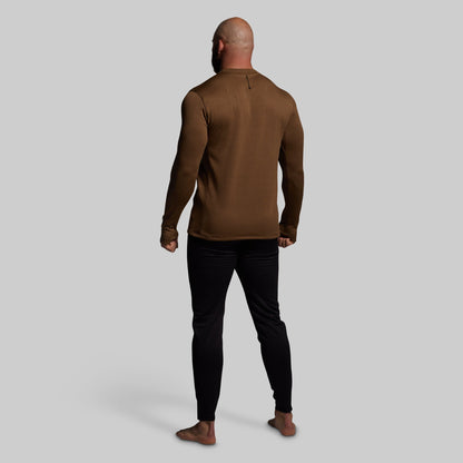 Man wearing a brown long-sleeve shirt and black pants on a gray background