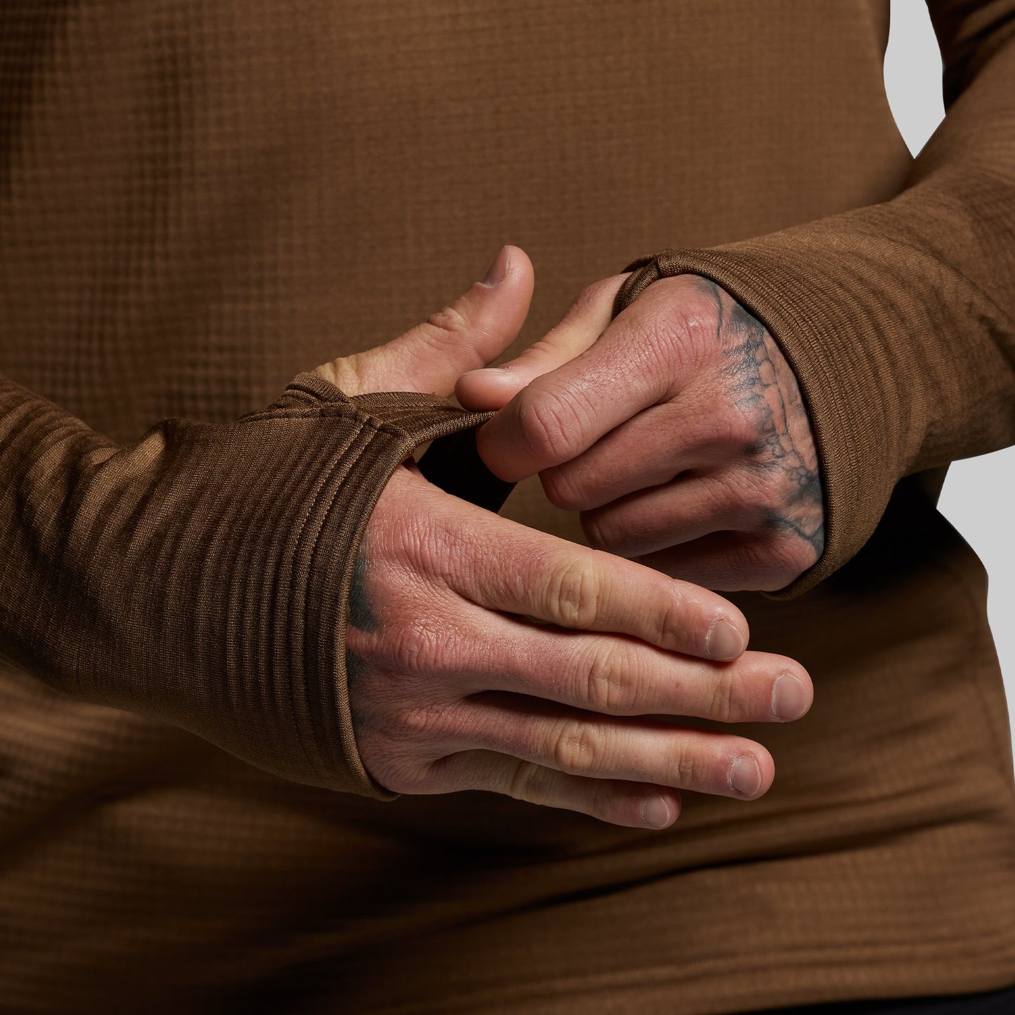 Close-up of a person wearing a brown long-sleeve shirt with tattooed hands.