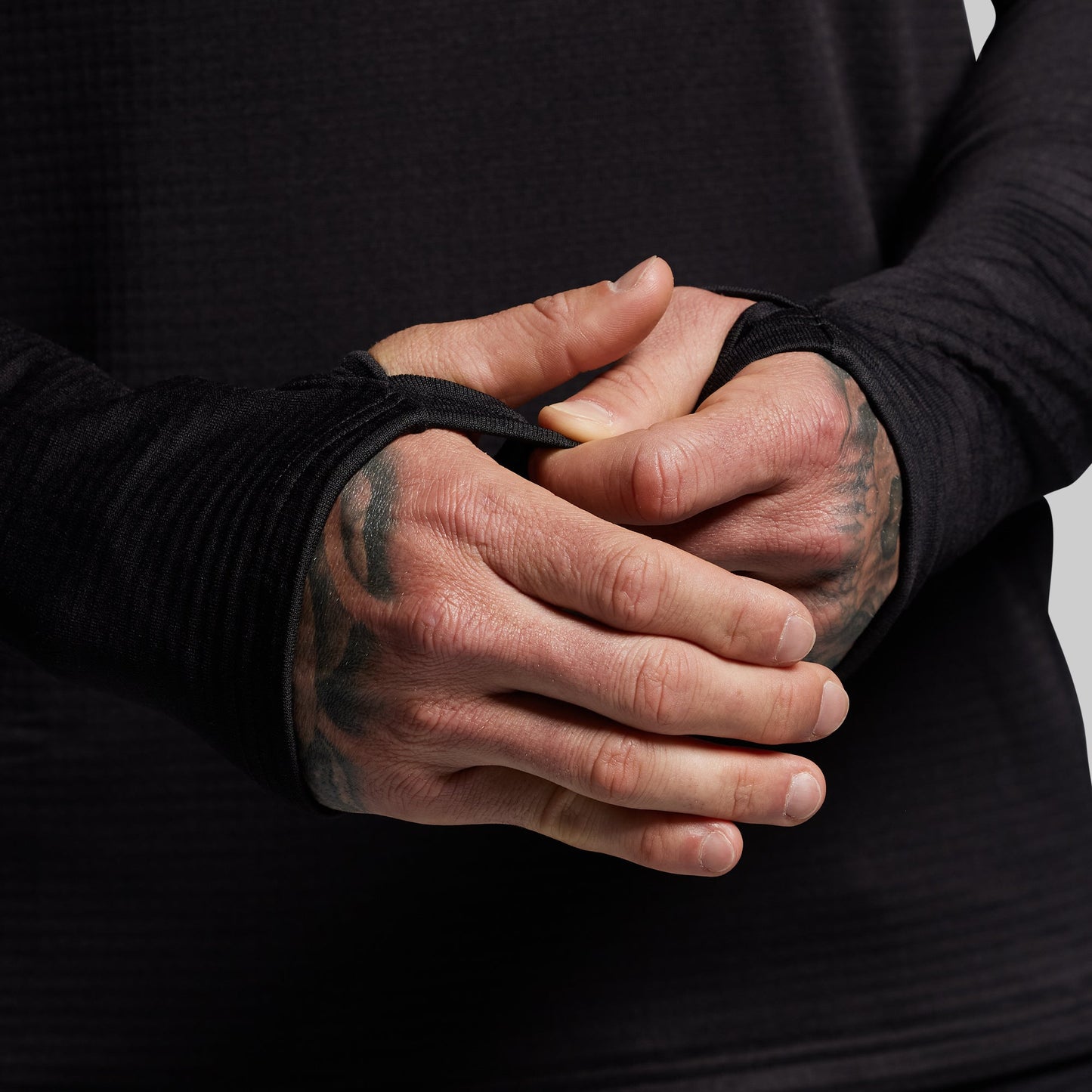 Person wearing black base layer long sleeve with thumbholes on a gray background