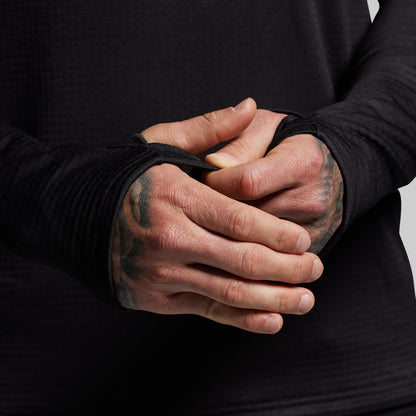 Person wearing black base layer long sleeve with thumbholes on a gray background