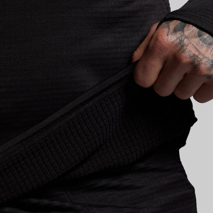 Person wearing a black textured base layer with a tattooed hand adjusting the hem.