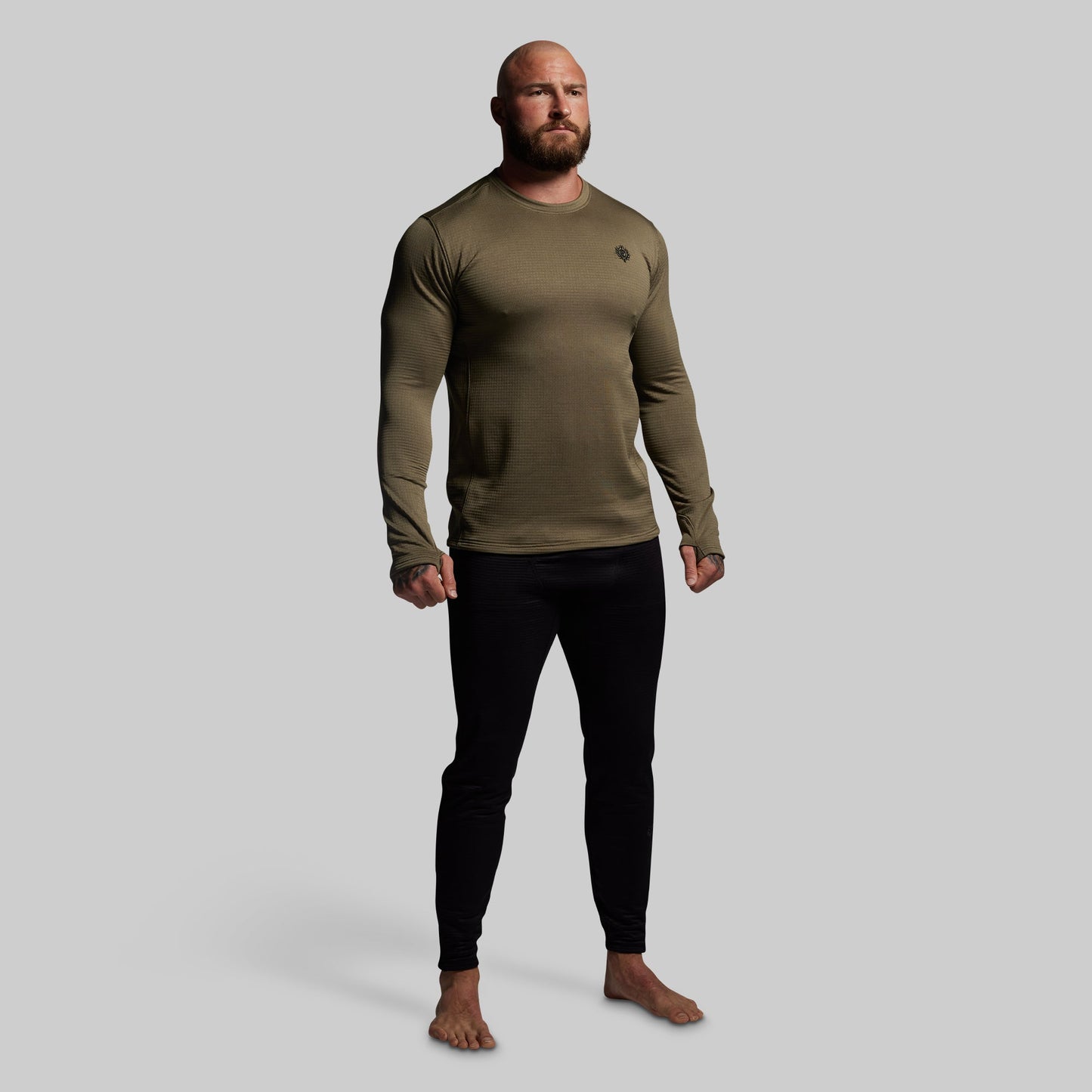 Man wearing an olive green long-sleeve shirt and black pants on a gray background