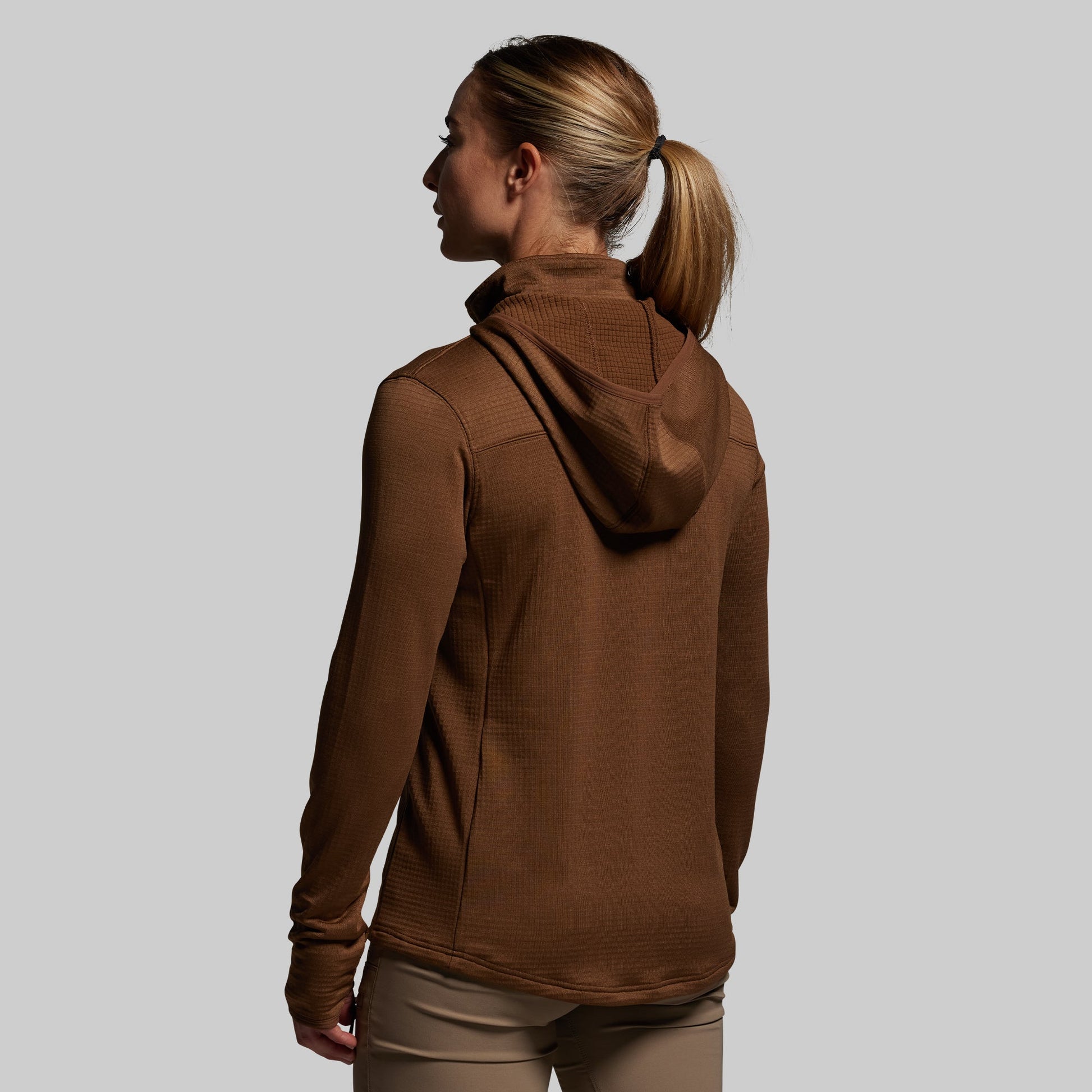 Woman wearing a brown hoodie against a plain background