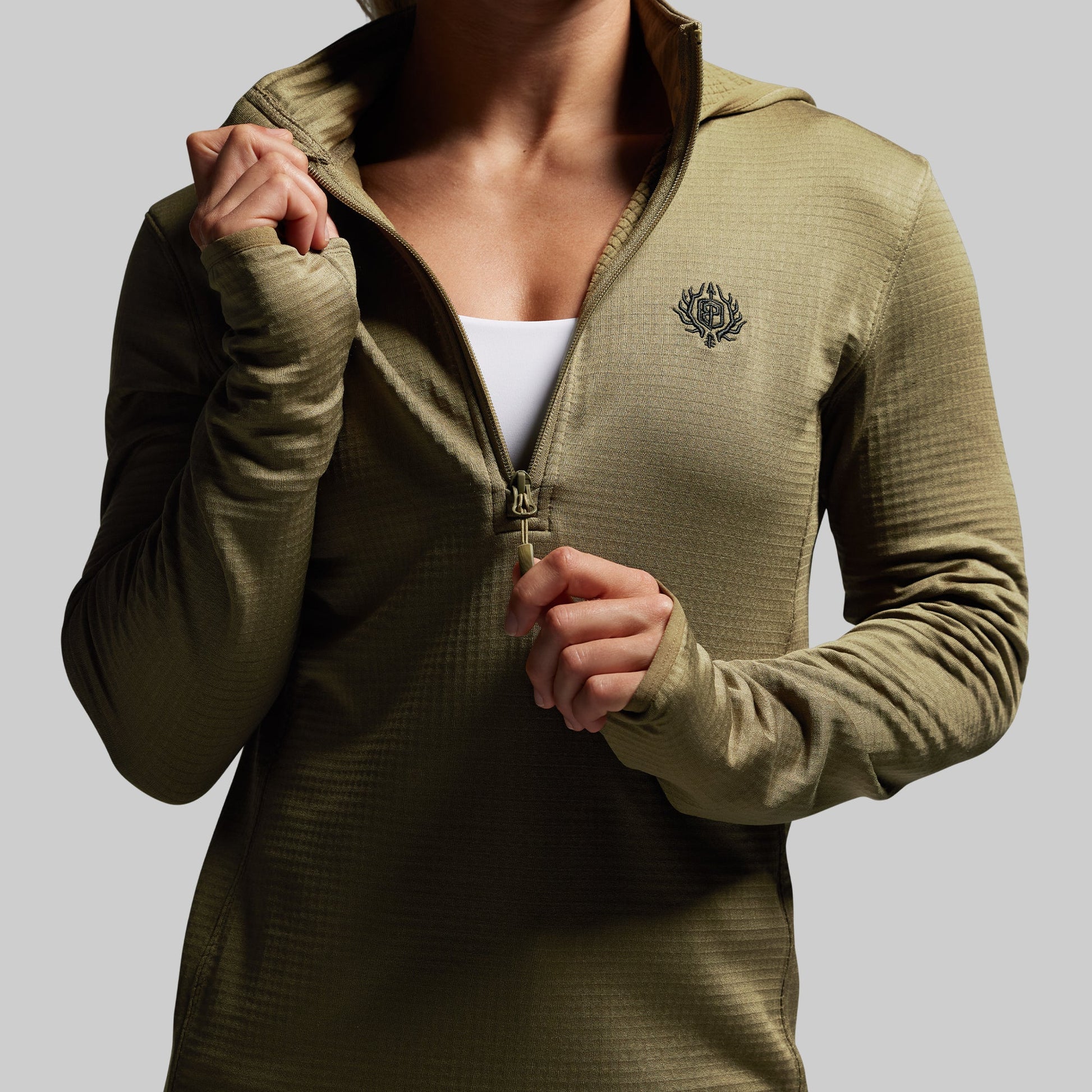 Person wearing a green half zip-up hoodie with a logo on a gray background