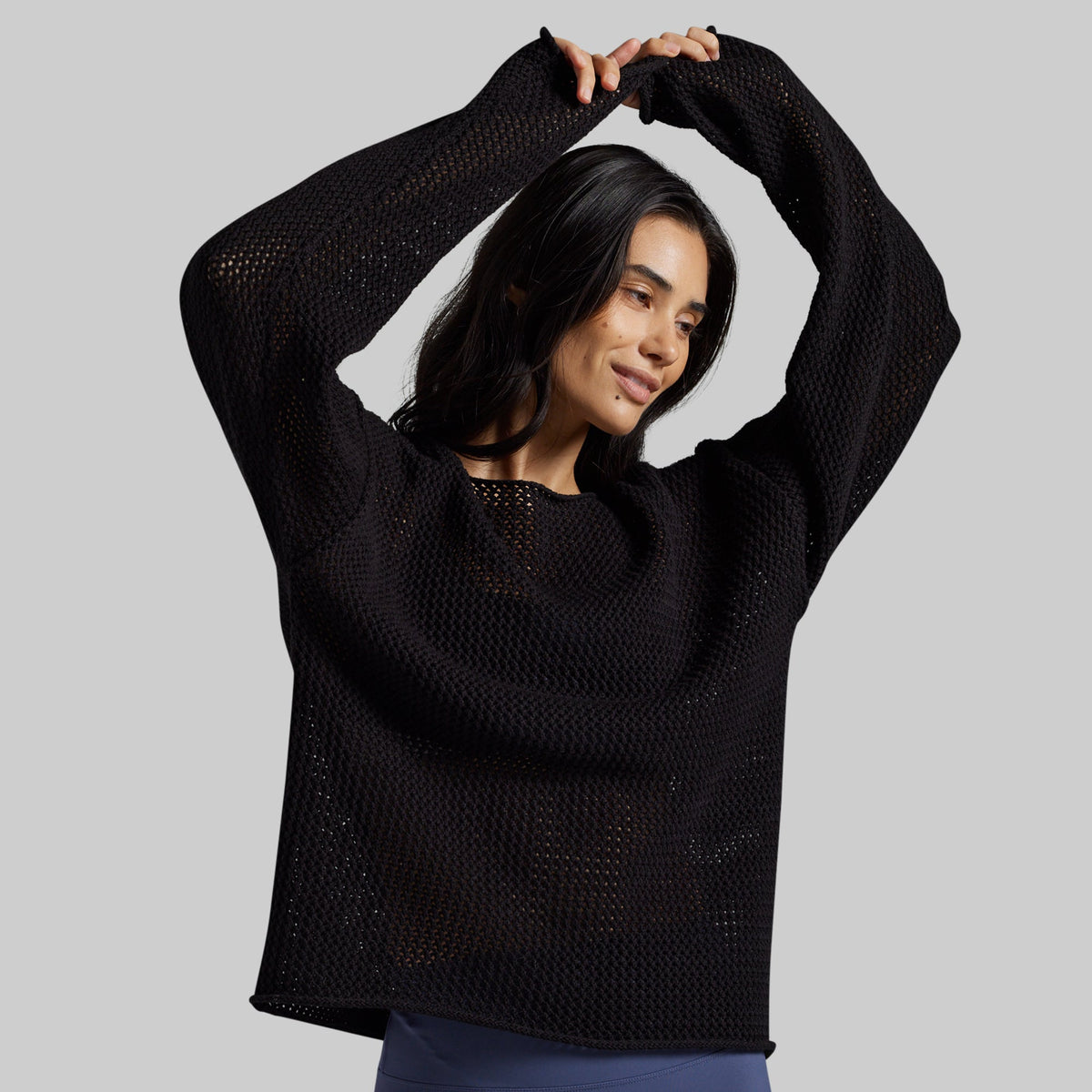 A woman modeling a black open-knit long-sleeve sweater against a solid gray background.
