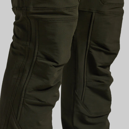 Close-up of dark olive green technical pants showing the leg construction, seam details, and pocket stitching against a neutral gray background.