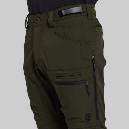 Close-up of olive green technical pants with multiple zippered cargo pockets, belt loops, and a dark belt, shown on a model against a light gray background.