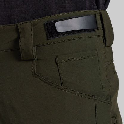 Close-up of the back waistband and pocket area of olive green outdoor pants, showing a black hook-and-loop patch with a silver metal bar, stitching, and belt loops.