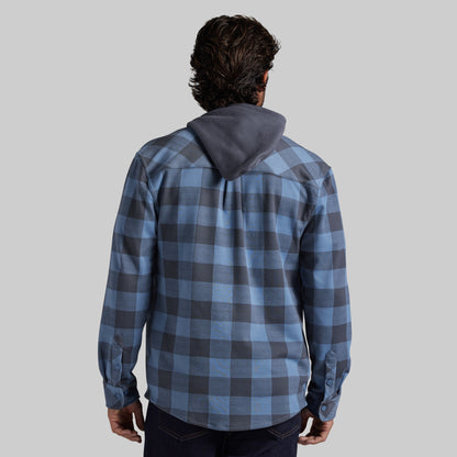 A man viewed from behind wearing a blue and gray plaid hooded shirt, set against a solid light gray background.