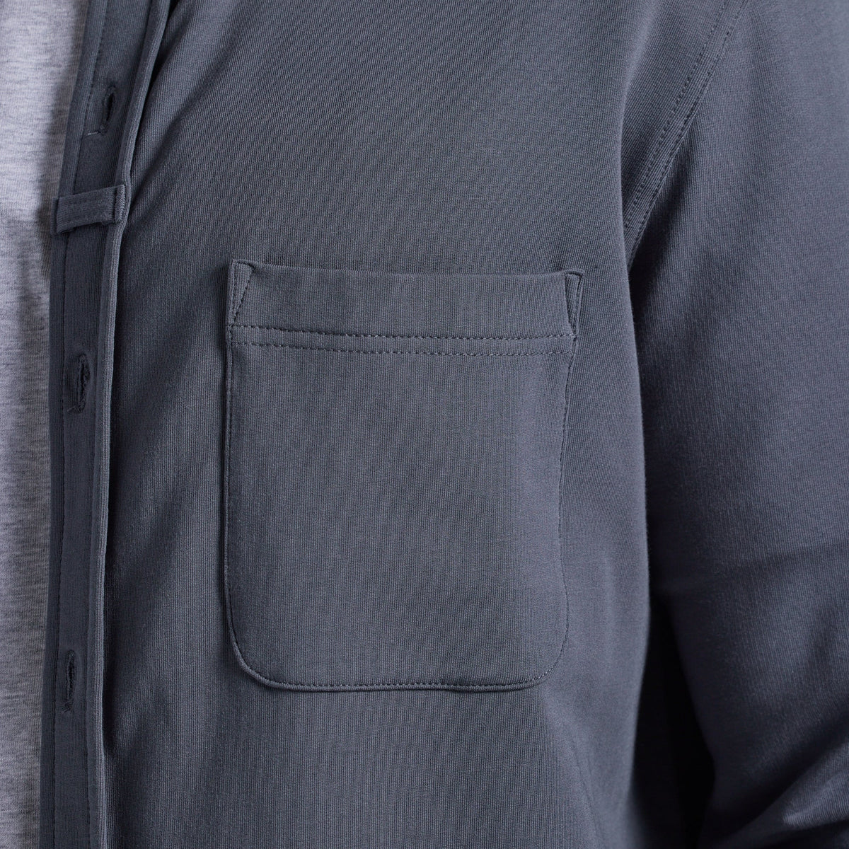 Close-up of a dark gray long-sleeve button-up shirt with a chest pocket, worn over a light gray undershirt.