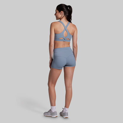 Woman wearing a gray sports bra and shorts set on a light gray background