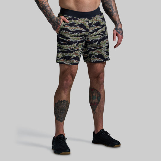 A person wearing camouflage patterned Versatile Shorts with a compression liner, standing with hands in pockets.