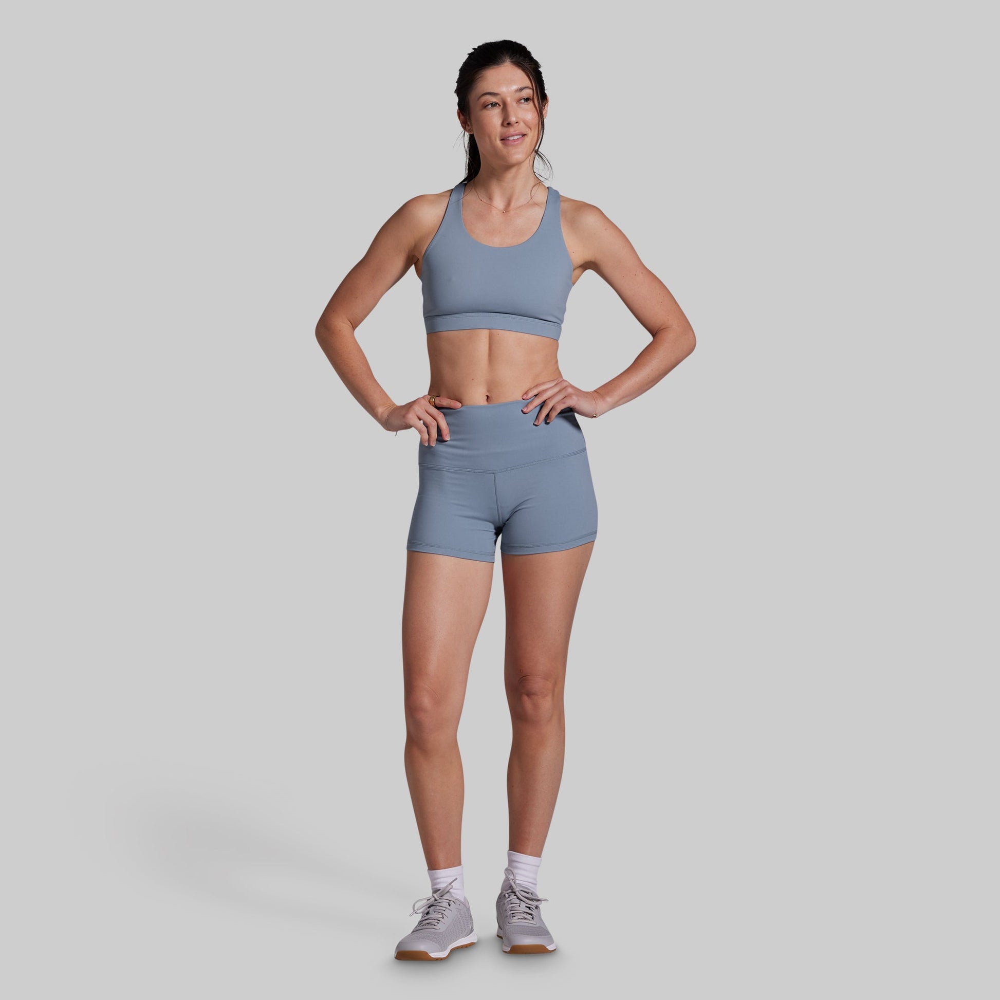 Woman wearing a gray sports bra and shorts on a light gray background