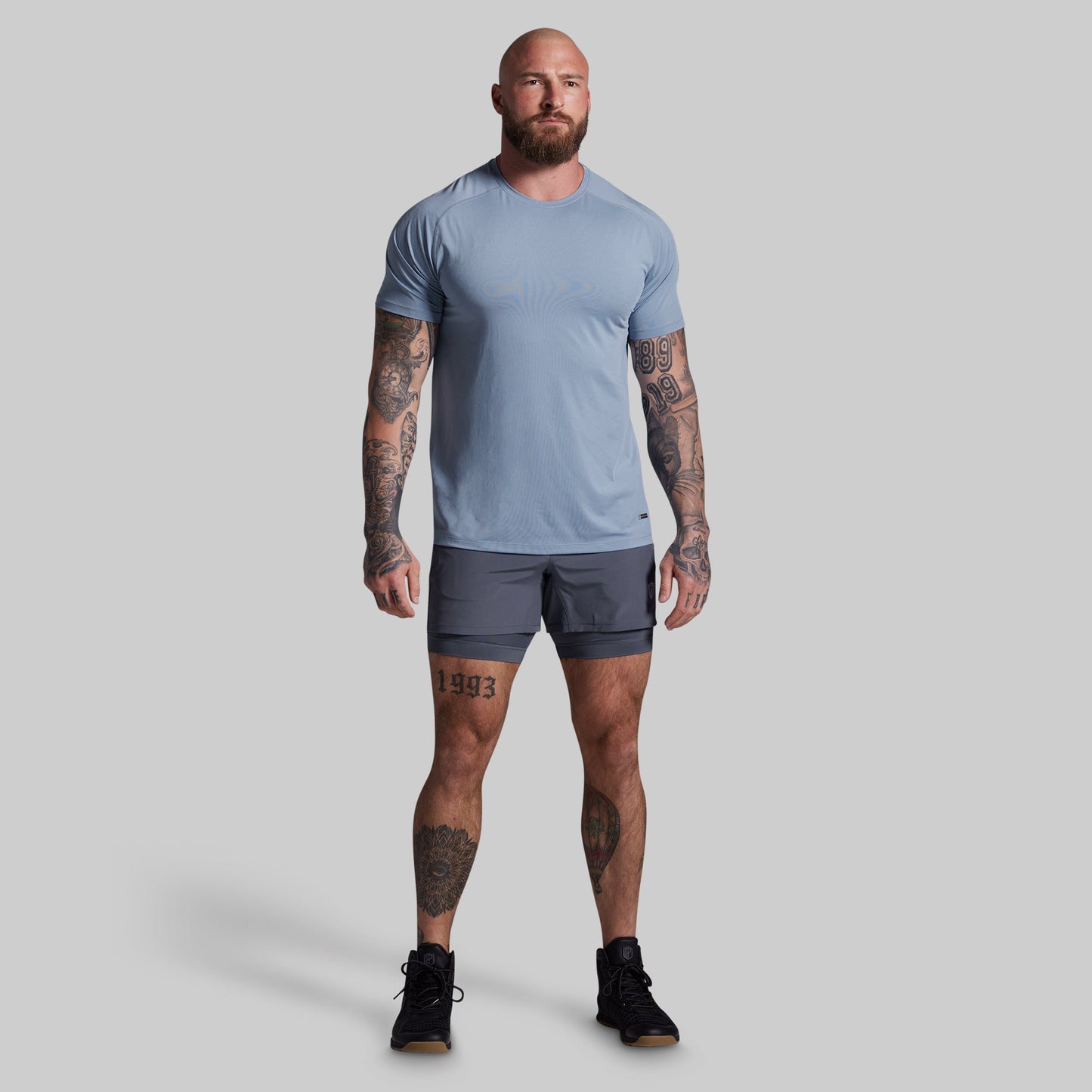 Man wearing a light blue t-shirt and dark gray shorts on a plain background