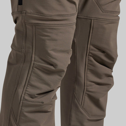 Close-up of a pair of technical outdoor pants in a warm grey color, showing the detailed stitching, reinforced knees, and fabric texture.