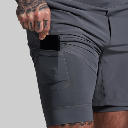 Person wearing gray shorts with a pocket, holding a phone.