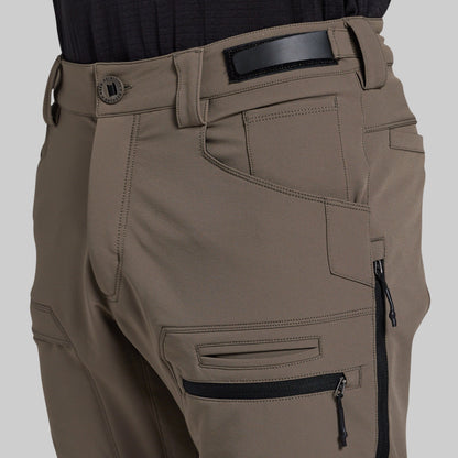 Close-up of a person wearing outdoor cargo pants in a storm grey color, featuring a black belt, belt buckle, and multiple zippered pockets.