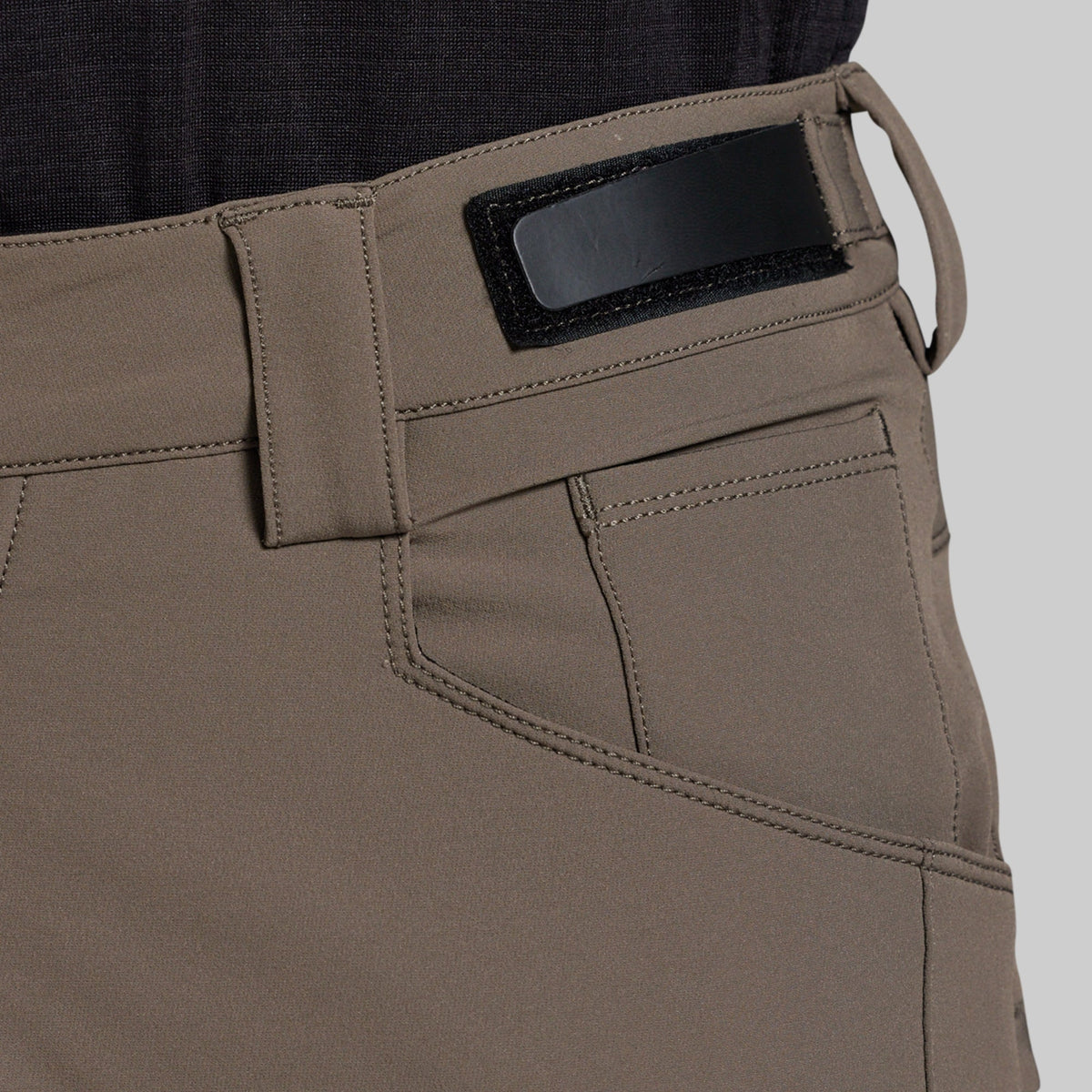 Close-up of a pair of outdoor pants in a storm grey color, showing the waistband with a black rectangular patch, belt loops, and a side pocket.