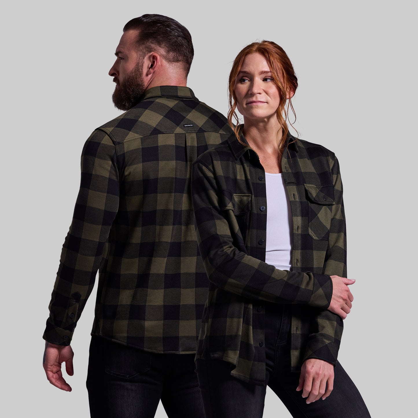 Two people wearing matching green and black plaid shirts against a plain background