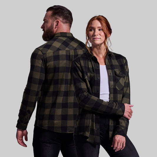 Two people wearing matching green and black plaid shirts against a plain background