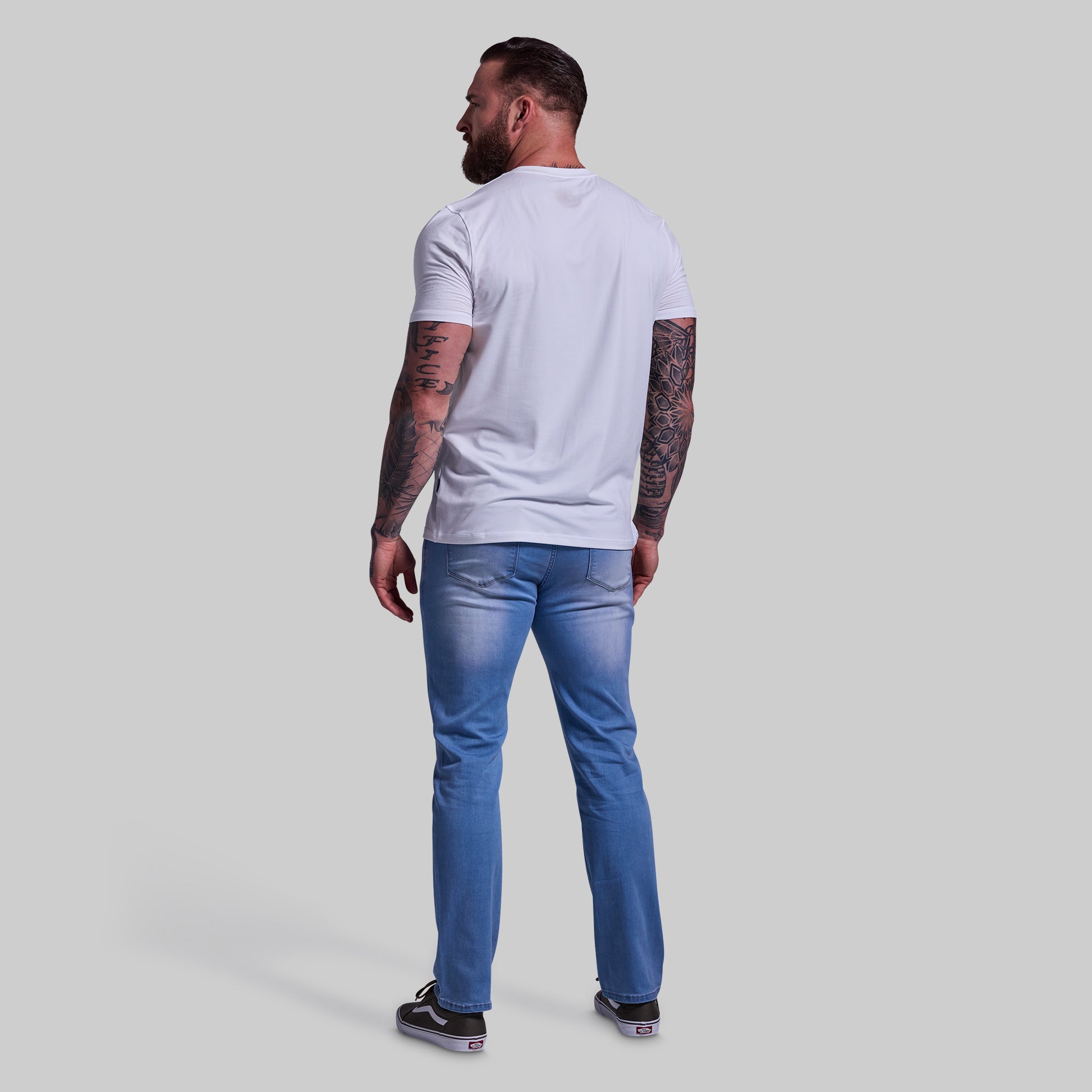 Man wearing a white t-shirt and blue jeans on a plain background