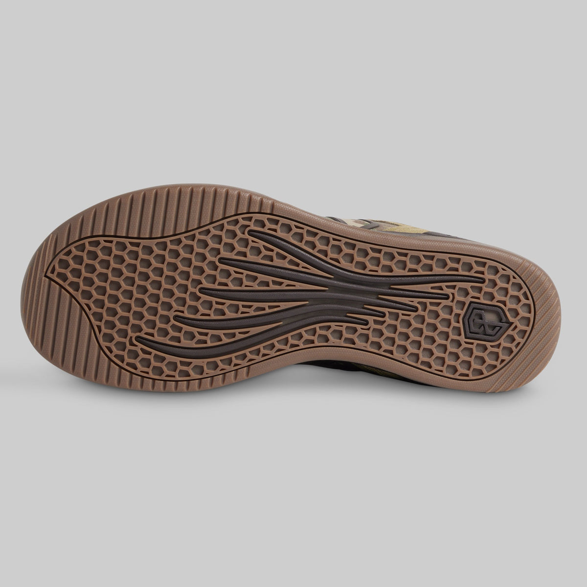 A close-up of a shoe's brown rubber outsole, showing a honeycomb tread pattern and black sculpted grooves, photographed on a solid gray background.
