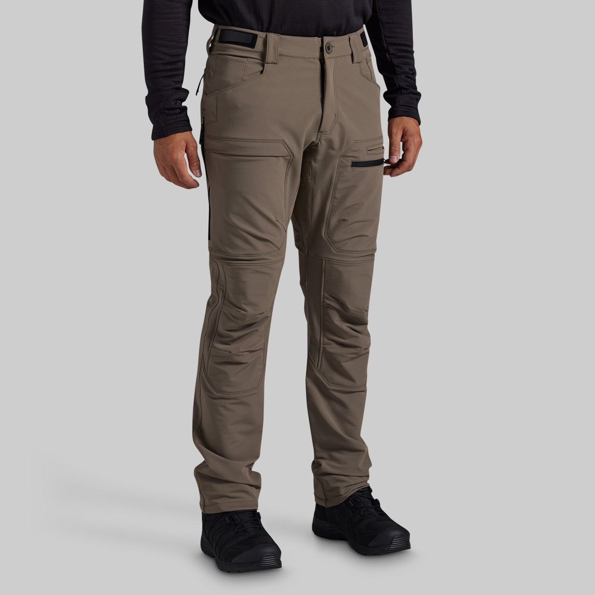 A man modeling grey technical cargo pants against a solid gray background.